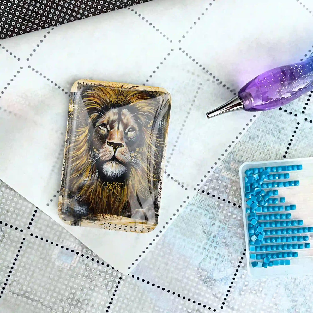 Löwen-Coverminder aus Glas für Diamond Painting auf einer Leinwand mit Stift und blauen Diamanten