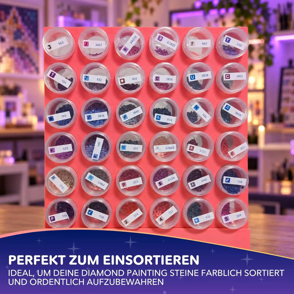 36 beschriftete Diamond Painting Aufbewahrungsdosen mit bunten Steinchen sortiert in pinkfarbener Halterung.