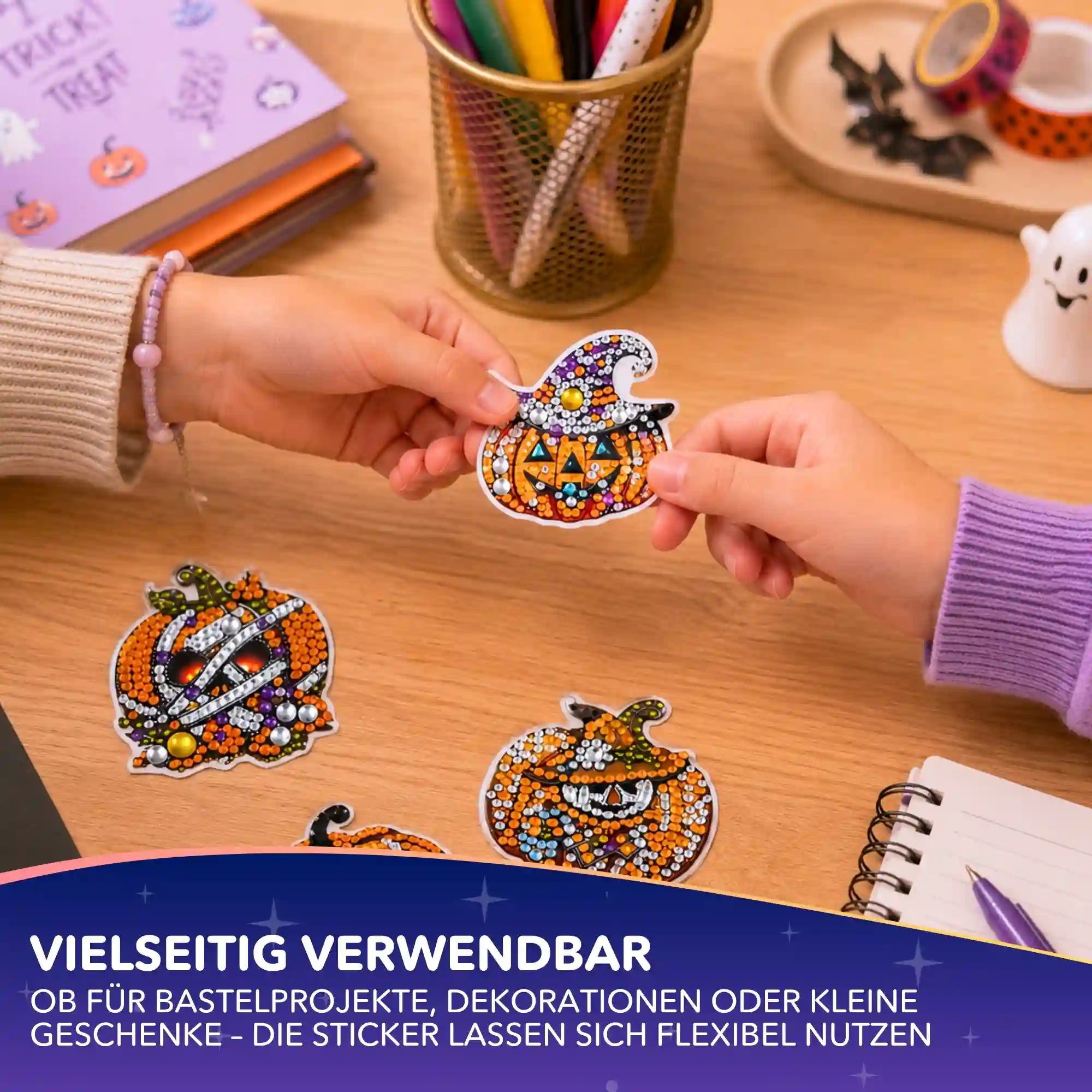 Hände halten funkelnde Halloween Diamond Painting Sticker mit Kürbis-Motiven auf einem Basteltisch